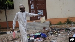 FILE - A man picks up an item belonging to a student at the site of a bomb blast in the university town of Zaria, Nigeria, July 7, 2015.