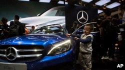 Chinese regulators have launched a series of anti-monopoly investigations of foreign automakers. In this photo taken Sunday, April 20, 2014, a child touches the latest model from Mercedes at an auto show in Beijing.