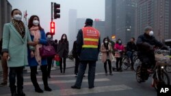 FILE - Pedestrians wearing mask against heavy pollution wait to cross a traffic junction in Beijing, China, March 16, 2015. 