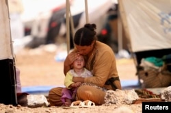 FILE - A refugee woman from the minority Yazidi sect, who fled the violence in the Iraqi town of Sinjar, sits with a child inside a tent at Nowruz refugee camp in Qamishli, northeastern Syria, Aug. 17, 2014.