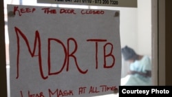 Un joven paciente con la potencialmente fatal MDR-TB en aislado un hospital en Sudáfrica y un cartel pide mantener la puerta cerrada y usar una máscara todo el tiempo.
