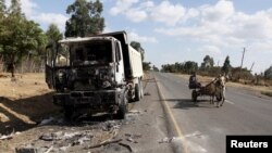 A man drives a horse-cart past the wreckage of a truck torched during recent demonstrations along the road in Holonkomi town, in Oromiya region of Ethiopia, Dec. 17, 2015. 