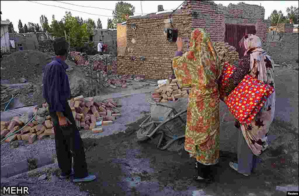 Earthquake victims stand near damaged houses in northwest Iran, August 12, 2012.