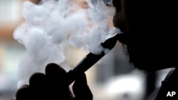 FILE - A smoker demonstrates an e-cigarette at Vape store in Chicago, April 23, 2014. A new study found that toxicity levels of e-cigarettes can fluctuate with the temperature, type and age of the device, a new study has found.