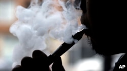 FILE - Daryl Cura demonstrates smoking an e-cigarette at Vape store in Chicago, April 23, 2014.