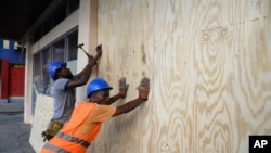 A worker nails a board to use on a storefront window as protection against hurricane Matthew in Kingston, Saturday, Oct. 1, 2016. One of the most powerful Atlantic hurricanes in recent history is also headed toward eastern Cuba and western Haiti.