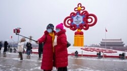 Women wearing face masks printed with a slogan for the Beijing Winter Olympics Games take a selfie with a decoration for the Winter Olympics Games in Tiananmen Square in Beijing on Jan. 20, 2022.