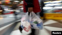 Seorang pelanggan membawa kantong plastik keluar dari supermarket di pusat Kota Beijing, China, 17 Maret 2011. (Foto: Reuters)