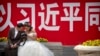 资料照：一对穿着婚礼服装的夫妇2018年5月19日在北京观看照相机背面的照片，身后是关于中国国家主席习近平的宣传口号。
