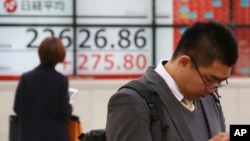 People stand by an electronic stock board of a securities firm in Tokyo, Dec. 3, 2018. Shares are advancing in Asia following the meeting between Presidents Donald Trump and Xi Jinping.