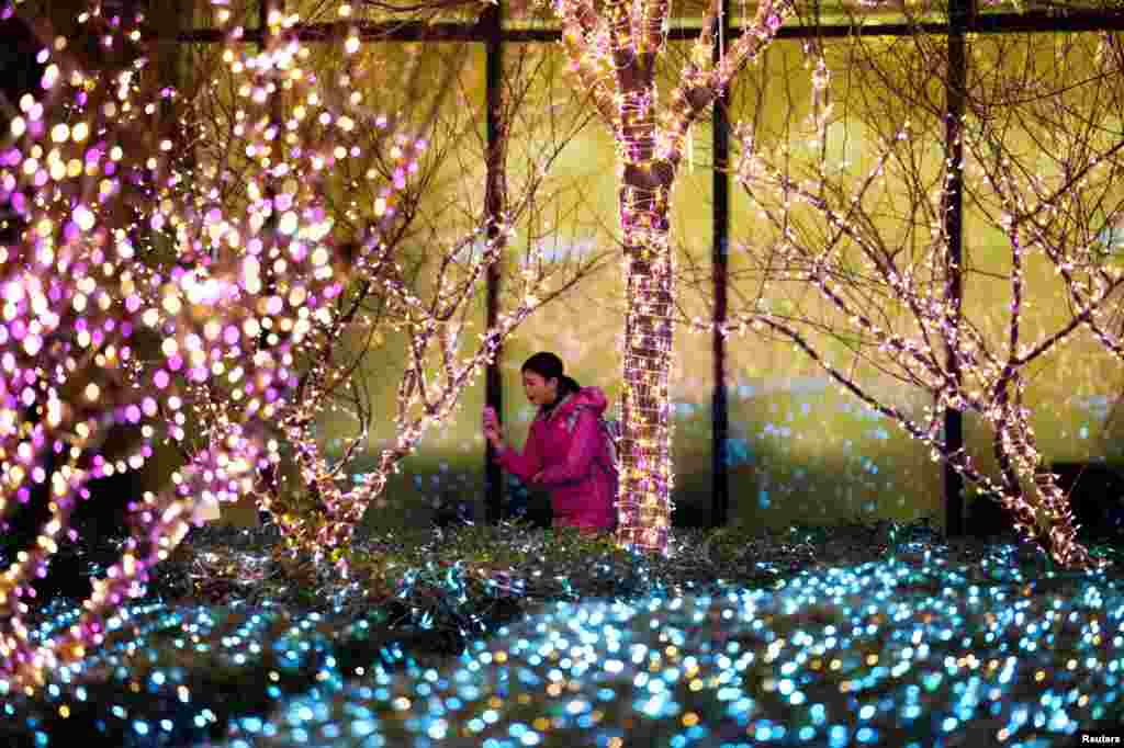 在中国北京一座办公楼前面，一位女孩走过满载圣诞节彩灯的树丛。
