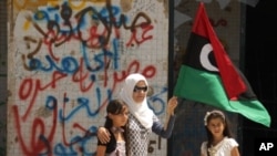 A Libyan woman holding the rebellion's flag tours with her daughters Moamer Kadhafi's destroyed headquarters of Bab al-Aziziya in Tripoli, August 31, 2011