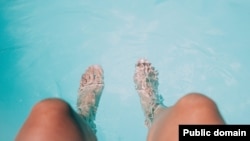 A woman rests at a swimming pool and cools her feet.