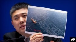 Huo Chuanlin, deputy director of the Department of Ecological and Environment Protection of China's State Oceanic Administration, holds a photo showing a rescue ship and an oil slick during a press conference about the Iranian oil tanker Sanchi, which exploded and sank after a collision in the East China Sea in January, at the Information Office of the Ministry of Transport in Beijing, Thursday, Feb. 1, 2018. Chinese officials say they are still debating whether to try to raise an Iranian oil tanker that sank last month with the loss of all 32 crew members.