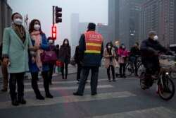 FILE - Pedestrians wearing masks to block out heavy pollution wait on traffic to cross a street in Beijing, China, March 16, 2015.