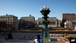 FILE - A woman sits on the near-empty campus at Columbia University in New York, March 9, 2020.