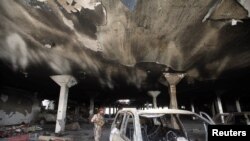 FILE - A security guard looks at a damaged car during a visit by human rights activists to a community hall that was struck by an airstrike during a funeral on October 8, in Sanaa, Yemen, Oct. 16, 2016. 