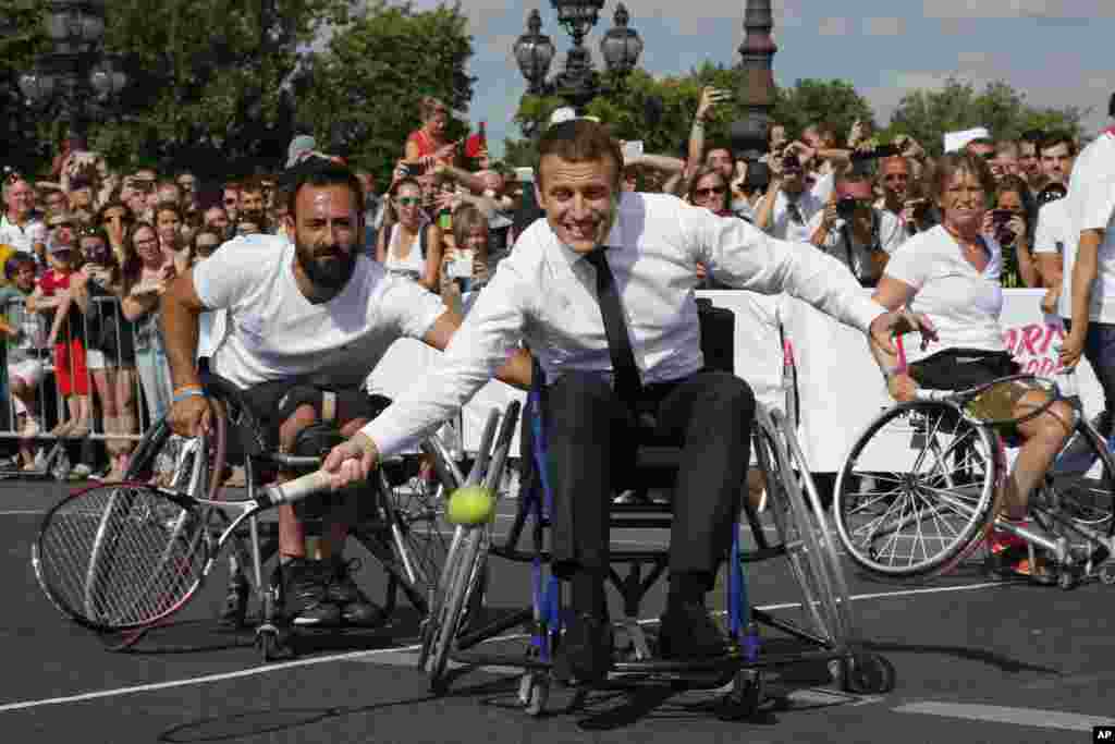 French President Emmanuel Macron returns the ball while sitting in a wheelchair as he plays tennis on the Pont Alexandre III in Paris, June 24, 2017.