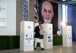 FILE - Afghan President Ashraf Ghani, center, walks toward a ballot box before casting his vote at Amani High School, near the presidential palace in Kabul, Afghanistan, Sept. 28, 2019.