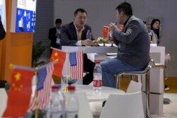 FILE - Visitors chat near American and Chinese flags displayed at a booth for an American company promoting environmental sensors during the China International Import Expo in Shanghai, Nov. 7, 2019.