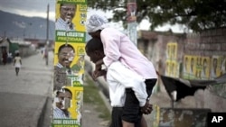 A man carrying a woman with cholera symptoms walks past campaign posters of presidential candidate Jude Celestin in Port-au-Prince (File)