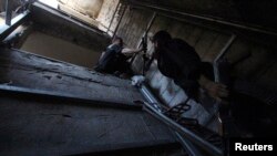 A rebel fighter hands a weapon to his fellow fighter as they move inside a building on the frontline in the Damascus suburb of Harasta, Syria, Aug. 24, 2014.