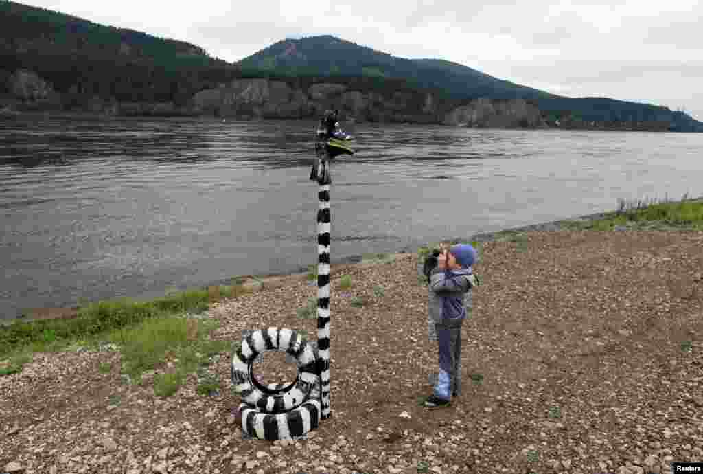 Seorang bocah laki-laki memotret instalasi seni di atas Sungai Yenisei di desa Ovsyanka, sekitar 24 kilometer dari kota Krasnoyarsk, Siberia di Rusia.