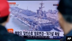 La gente ubicada en la estación de trenes de Seúl en Corea del Sur, ve un programa de noticias de televisión que muestra una imagen de archivo del portaaviones USS Carl Vinson.