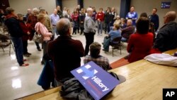 A campaign sign for Democratic presidential candidate Hillary Clinton sits behind a group of Clinton supporters during a Democratic party caucus in Nevada, Iowa, Feb. 1, 2016. 