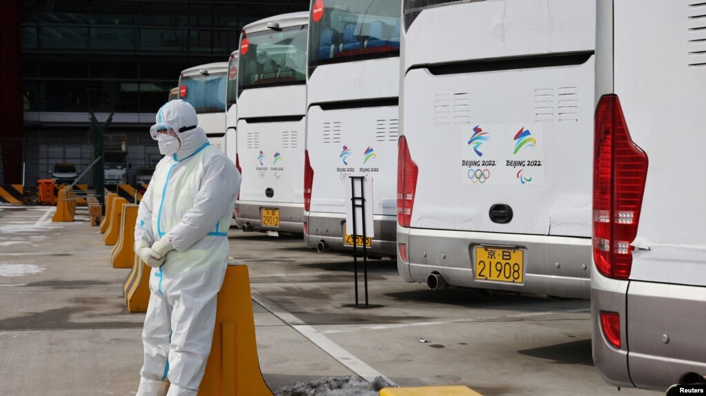 2022北京冬奥会一位身穿防护服的工作人员，他身后是专门接送冬奥会人员的大巴士。(photo:VOA)