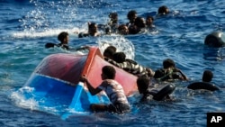 Migranti plivaju pored prevrnutog drvenog čamca tokom spasilačke operacije španske nevladine organizacije Open Arms na jugu italijanskog ostrva Lampeduza u Sredozemnom moru, 11. avgusta 2022.