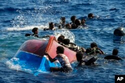 FILE - Para migran berenang di samping perahu kayu mereka yg terbalik Ketika akan diselamatkan dari LSM Spanyol Open Arms di laut Mediterania, selatan pulau Lampedusa Italia, 11 Agustus 2022. (AP/Francisco Seco, file)