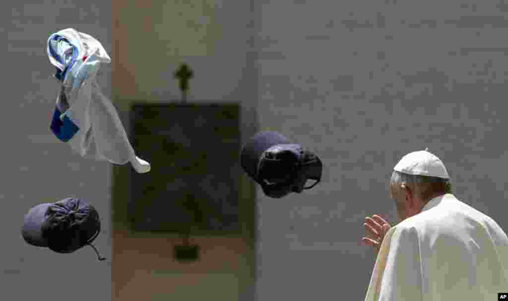 Faithful throw in the air a jersey and two hats as Pope Francis leaves at the end of his weekly general audience in St. Peter&#39;s Square at the Vatican.