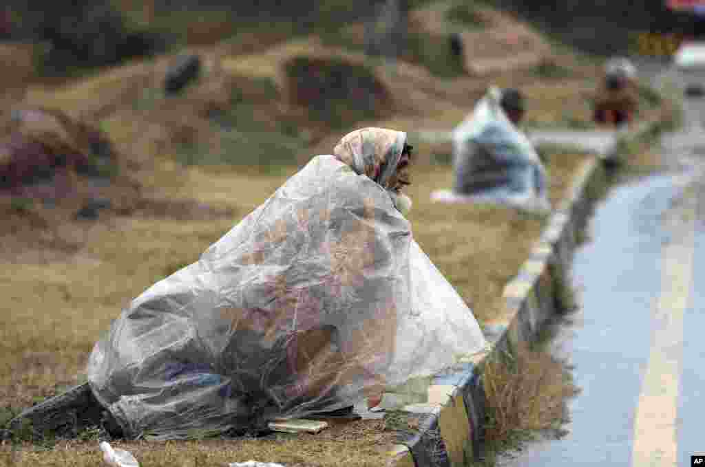 Men wait to receive donations from others as they cover themselves with plastic sheets as rain falls in Islamabad, Pakistan, Jan. 5, 2022.