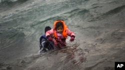 A man carries a child as they try to reach a shore after falling into the sea while disembarking from a dinghy on which they crossed a part of the Aegean sea with other refugees and migrants, from Turkey to the Greek island of Lesbos, Jan. 3, 2016.