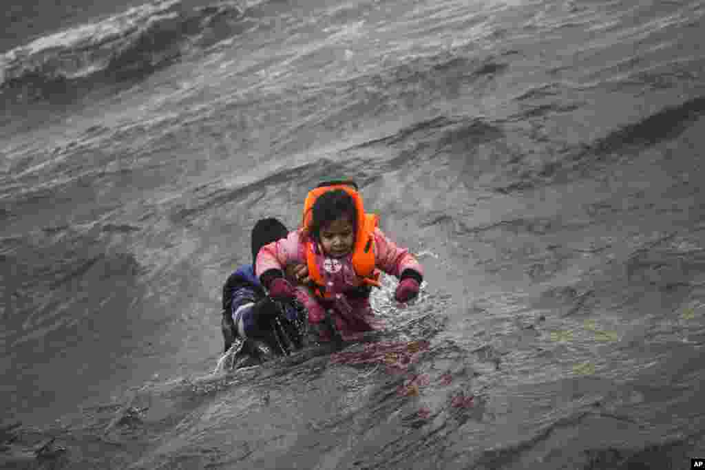 Seorang pria menggendong anaknya saat berusaha mencapai pantai setelah jatuh ke laut ketika turun dari kapal karet yang membawa mereka menyeberangi Laut Aegea bersama pengungsi dan migran lainnya, dari Turki ke pulau Lesbos, Yunani.