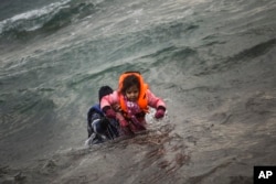 FILE - A man carries a child as they try to reach a shore after falling into the sea while disembarking from a dinghy on which they crossed a part of the Aegean sea with other refugees and migrants, from Turkey to the Greek island of Lesbos, Jan. 3, 2016.