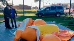 Un policía y un hombre no identificado, de pie junto a un globo con forma de caricatura de Donald Trump, desinflado por una persona en el Parque Monnish en Tuscaloosa, Alabama, el sábado 9 de noviembre de 2019. (Stephanie Taylor/The Tuscaloosa News via AP)
