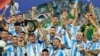 FILE - Argentina's Lionel Messi, holding the Copa America trophy, celebrates with teammates their victory over Colombia in the Copa America final soccer match in Miami Gardens, Fla., July 15, 2024. 