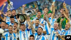 FILE - Argentina's Lionel Messi, holding the Copa America trophy, celebrates with teammates their victory over Colombia in the Copa America final soccer match in Miami Gardens, Fla., July 15, 2024. 