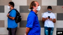 People wear face masks to protect against the coronavirus as they keep their distance in a queue at a supermarket during a mandatory confinement, in San Juan, Puerto Rico on April 7, 2020.