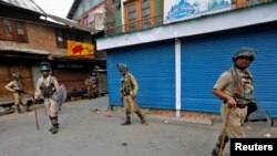 Indian policemen stand guard in front of the closed shops during a curfew in Srinagar, July 13, 2016. 