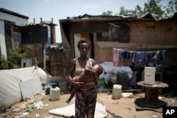 In this Oct. 20, 2017 photo, Simone Batista holds her 1-year-old Arthur outside her shack in the Jardim Gramacho slum of Rio de Janeiro, Brazil, one year after she was cut from the "Bolsa Familia" government subsidy program