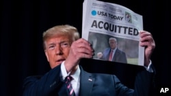 President Donald Trump holds up a newspaper with the headline that reads "ACQUITTED" at the 68th annual National Prayer Breakfast, at the Washington Hilton, Feb. 6, 2020, in Washington.