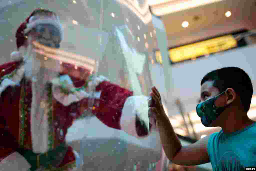 Abilio da Cruz Pinto, de 77 a&#241;os, vestido como un Pap&#225; Noel dentro de una burbuja de pl&#225;stico, saluda a un ni&#241;o en un centro comercial en medio del brote de la enfermedad por coronavirus en Brasilia, Brasil, el 15 de diciembre de 2020. [Reuters].