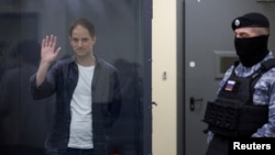 ARCHIVO - El reportero del Wall Street Journal, Evan Gershkovich, detenido por cargos de espionaje, saluda detrás de una pared de vidrio de un recinto para los acusados ​​mientras asiste a una audiencia judicial en Moscú, Rusia, el 23 de abril de 2024.