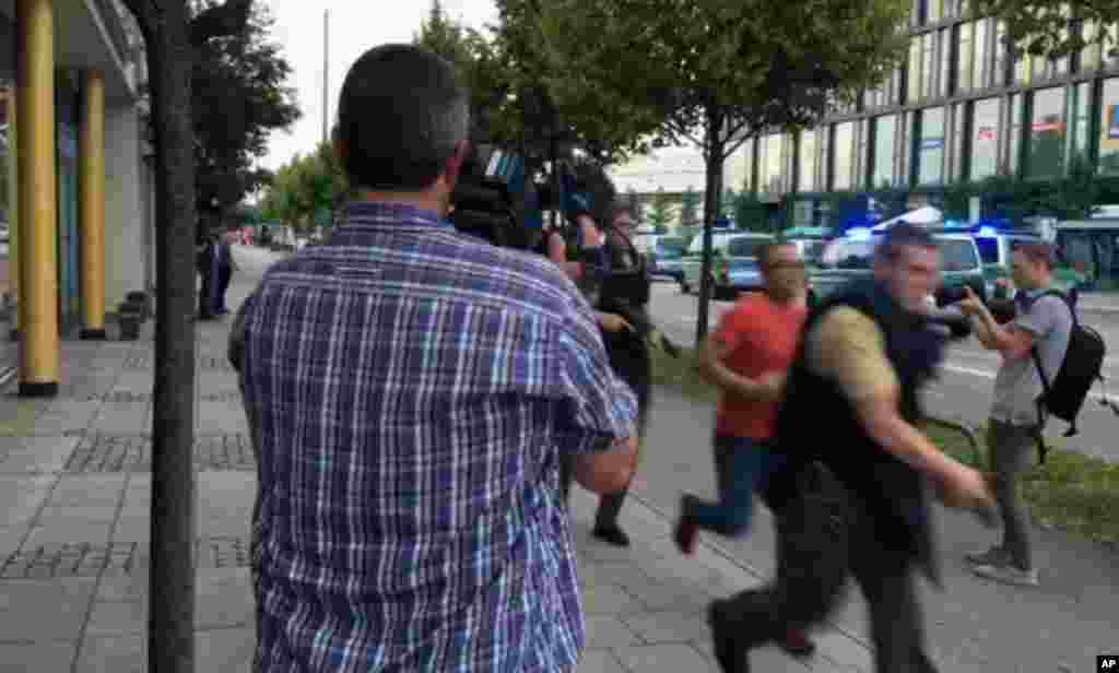 Armed police move past onlooking media responding to a shooting at Olympia Einkaufszentrum shopping center, July 22, 2016.