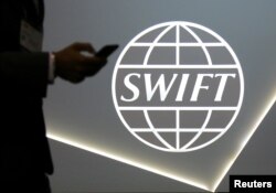 FILE - A man using a mobile phone passes the logo of global secure financial messaging services cooperative SWIFT at the SIBOS banking and financial conference in Toronto, Ontario, Oct. 19, 2017.