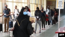 FILE - Travelers wearing masks walk at Jomo Kenyatta International Airport in Nairobi, Aug. 1, 2020. Kenyan authorities say that since November 2021, at least 23 domestic workers have died while working in the Middle East, many in Saudi Arabia. 
