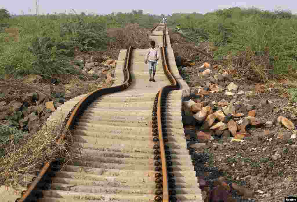 Seorang penduduk desa berjalan di trek kereta yang rusak akibat hujan deras dekat desa Patdi di Gujarat, India.